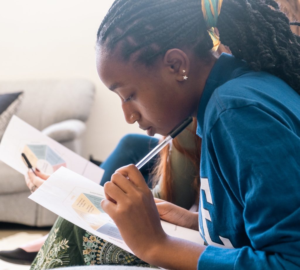 Student carefully reviewing study materials and taking notes, demonstrating focused preparation and independent learning skills before college.